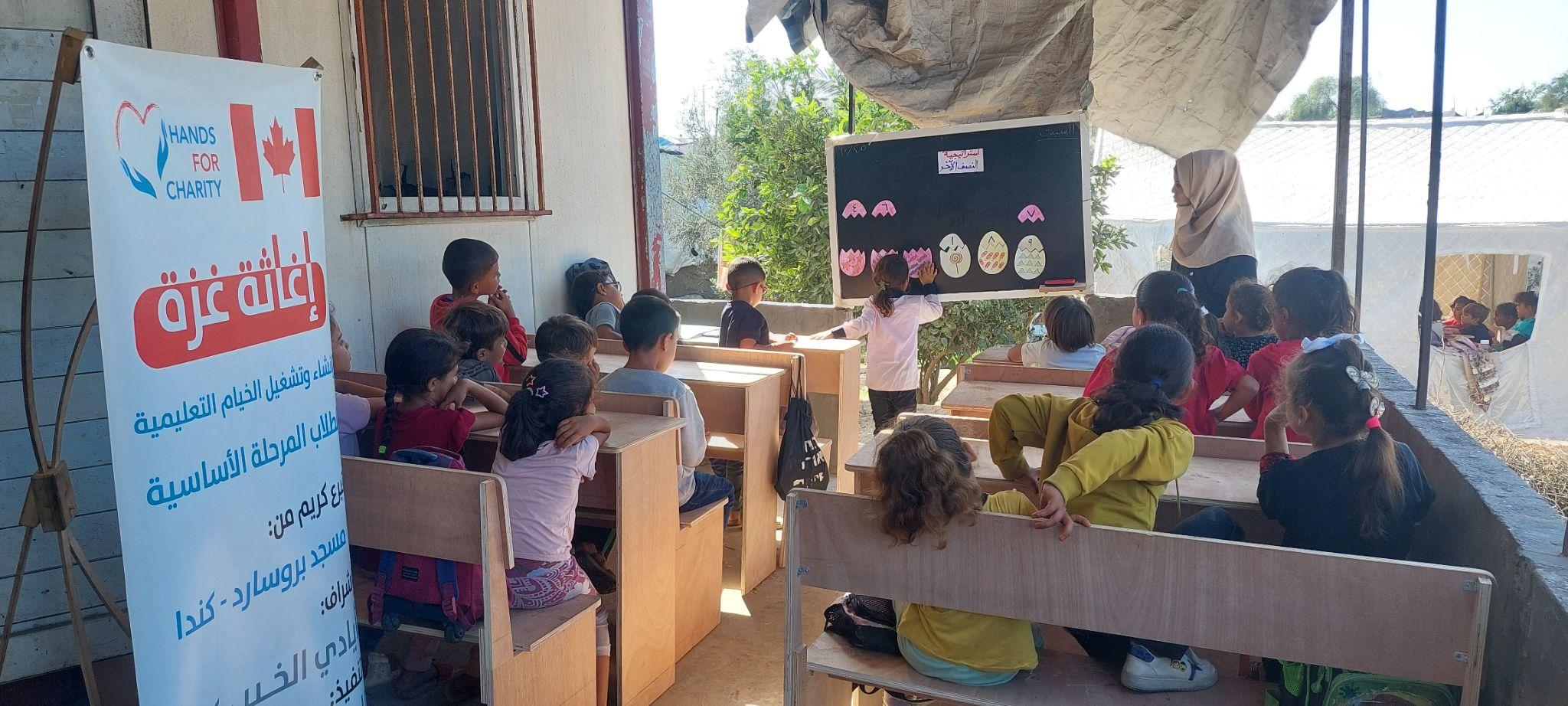 Children learning in an outdoor classroom tent run by Hands for Charity in Gaza